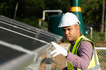 Young asian electrical engineer standing in front of Solar cell panels farm. He checking and...