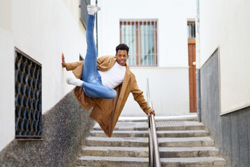 Young black man jumping for joy over a handrail in the street.