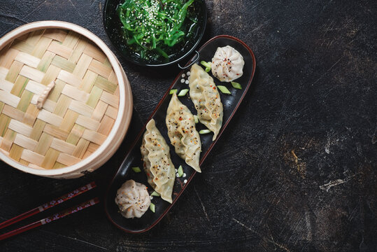 Chinese steamed dumplings with seaweed salad over dark brown stone background, horizontal shot with copyspace, above view