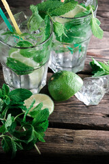 Mojito cocktails on a rustic wooden desk background. Two natural mojito cocktails with mint leaves, ice cubes, and lime on a wooden table.