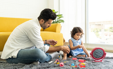 Fototapeta premium The curly-haired daughter happily sits on the rug with her father in the living room of the house. 