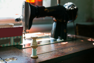 Skeins of thread on wooden spools are collected in a cardboard box on a vintage sewing machine.
