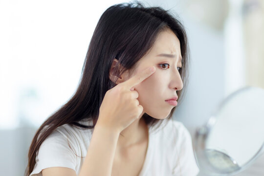 Young Woman Looking At  Mirror And Checking The  Crow's Feet Problem At Home