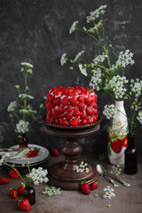 Strawberry red cake on a tall wooden stand. Beautiful cake with berries on a table with summer flowers.