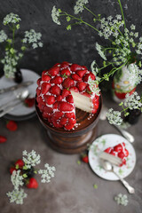 Strawberry red cake on a tall wooden stand. Beautiful cake with berries on a table with summer flowers.