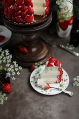 Strawberry red cake on a tall wooden stand. Beautiful cake with berries on a table with summer flowers.