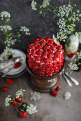 Strawberry red cake on a tall wooden stand. Beautiful cake with berries on a table with summer flowers.