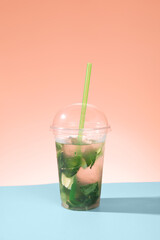 homemade non-alcoholic mojito on a blue table and pink background. summer refreshing drink with ice and a straw
