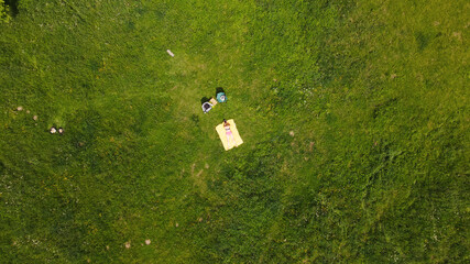Woman sunbathes on a green meadow. Lying on his stomach, on a yellow rug. Aerial photography.