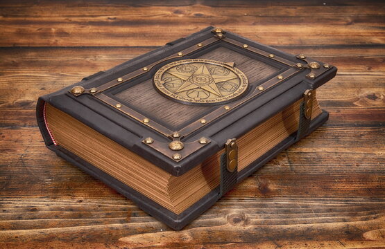 Large vintage black leather book with magical geometrical symbols in the center of rich decorated cover lay down on old wooden table