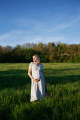 Fototapeta na wymiar pregnant woman on a green meadow walking with a bouquet of flowers