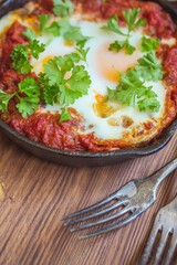 Shakshuka - fried eggs with vegetables in iron cast on wooden table
