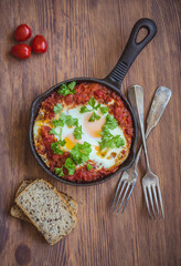 Shakshuka - fried eggs with vegetables in iron cast on wooden table