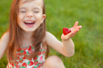 The happy girl sits on the grass and holds strawberries and laughs. Emotions, happiness, laughter, joy. summer, outdoor recreation. Place for text.