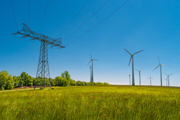 Panoramic view over beautiful farm landscape with meadow field with different flowers, wind turbines to produce green energy and electrical power lines in Germany, Summer, at blue sky and sunny day.