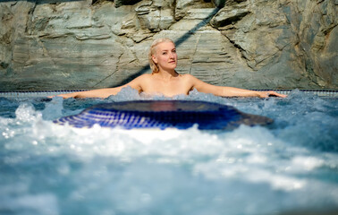 beautiful young cute sexy blonde woman with arms stretched to the side in the bubbling water of Spa Wellness whirlpool, copy space