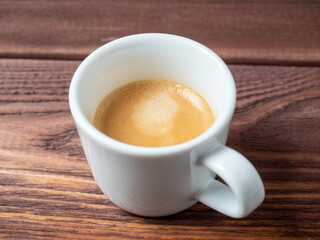 a white cup with a delicious and aromatic espresso on a wooden background. side view