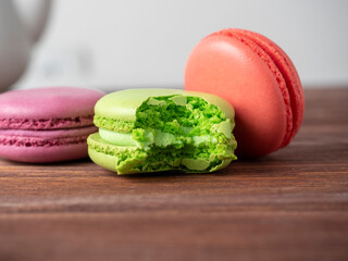 Colorful macaroons on a brown wooden background. One of them is bitten off. Delicious dessert