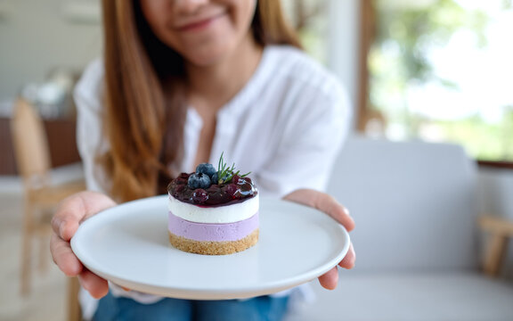 Closeup image of a young asian woman holding and showing a plate of blueberry cheesecake