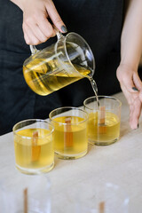 The girl pours wax into glass glasses with wicks.