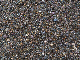 The texture of dark, multicolored wet sea pebbles from the coast in full screen. Large and small smooth stones. The concept of the background is about a summer vacation.