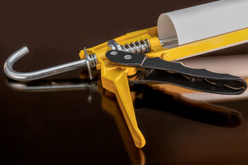 Glue and sealant gun with reflection on black background. Construction tool for silicone and glue. Close-up.