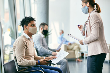 Young black candidate talking to human resource manager while waiting for job interview during COVID-19 pandemic.