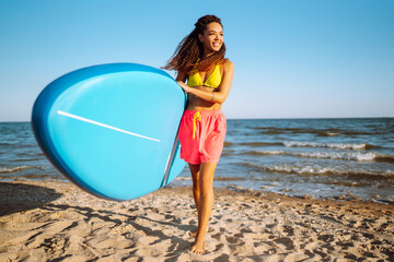 Beautiful sexy woman with glanders at the beach. Woman surfer walks with a board on the sandy beach. Healthy active lifestyle. Surfing. Summer vacation. Extreme sport. Travel, weekend,  lifestyle.