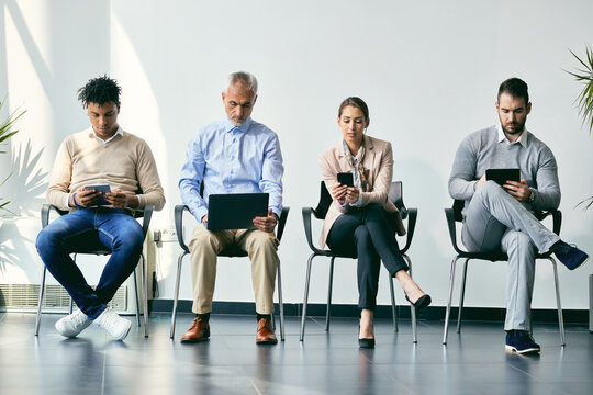 group of diverse entrepreneurs waiting for job interview and using wireless technology in a hallway.