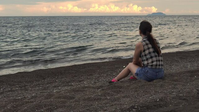 Young woman sitting on the beach and enjoying the view of the seascape. 4k footage
