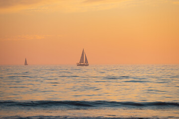Obraz na płótnie Canvas Sailing yacht on sunrise. Calm sea with sunset sky and sun through the clouds over. Ocean and sky background, seascape.