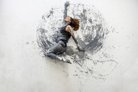 Young woman in gray shirt lies dancing dances on the floor elegantly decorative. Creative, abstract expressive body art and painting.