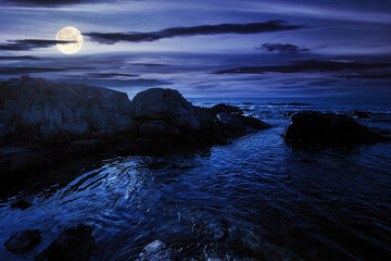 sea coast scenery at night. boulders in the calm water. few clouds on the sky in full moon light....
