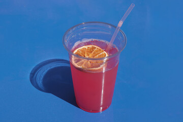 pink cocktail on a blue background with a dried slice of orange