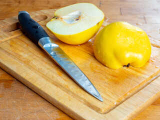 Cut in half yellow quince and a knife with water drops on a wooden cutting board close-up. Copy...