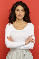 Obraz premium Portrait of confident young woman standing over red studio wall background with crossed arms. Millennial female businesswoman in white clothes with folded hands look serious smile and bossy in camera