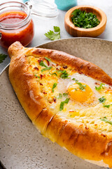  A traditional dish of Georgian cuisine, Adjarian khachapuri with cheese and egg and spicy tomato sauce adjika on the plate vertical photod close up