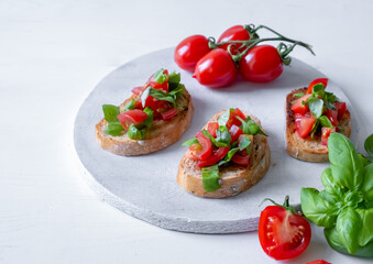Three bruschetta with tomatoes and fresh basil on a white wooden board
