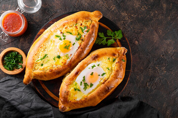  A traditional dish of Georgian cuisine, Adjarian khachapuri with cheese and egg and spicy tomato sauce adjika on the dark background top view, free space for text