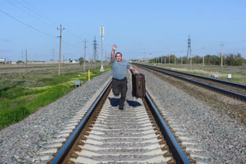 Man with suitcase runs along the railroad. Traveler missed his train and is catching up with him