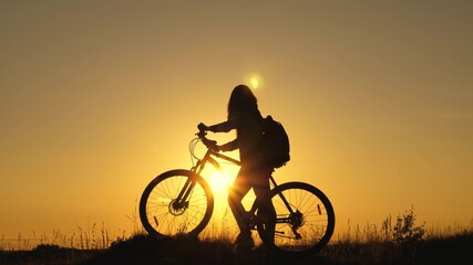 Fototapeta na wymiar Young woman tourist walks on a bike, enjoying the nature, fresh air in summer park. A free girl travels on a bike, rests, looks at the sunset and enjoys the sun. Adventure and travel concept.