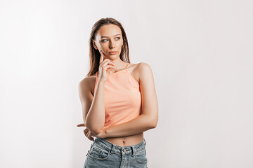 Beautiful young girl unhappy frown and thinks on gray isolated background. Serious woman looks to the side and holds hand to face