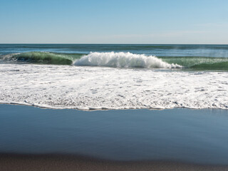 View from the Khalaktyrsky beach to the Pacific Ocean against the background of the blue sky. On the shores of the black sand beach, big and small waves break. Kamchatka Peninsula, Russia.