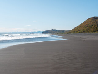 View from the Khalaktyrsky beach to the Pacific Ocean against the background of the blue sky. On the horizon of the black sand beach, cliffs and ocean waves are visible. Kamchatka Peninsula, Russia.