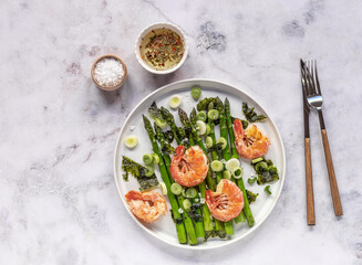 Delicious healthy salad of green asparagus, shrimps, onion, and nori on the white plate. Clean eating. Seasonal food. Top view, copy space for the recipe.