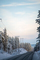 Blacktop road through a winter forest landscape with power lines and blue sky