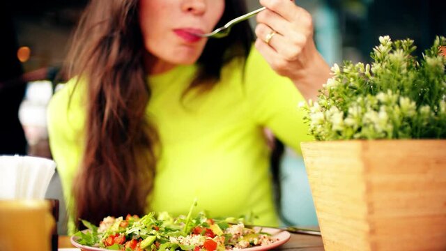 Uncognizable beautiful young woman eats vegan salad in a cafe. Healthy eating concept