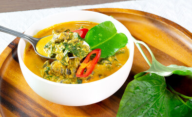 Curry periwinkle with cha ploo leaf in white bowl and Cha polo leaf put in the wooden tray thai food