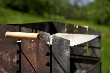Rusted grill stove stands in the green nature. Grate with wooden handles. Side view.