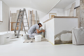 plasterer man at work, take the mortar from the bucket with trowel to plastering the wall of interior construction house site and wear helmet, panoramic image